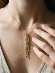 Gold-plated brass spoon talisman shown worn on a model, featuring two faceted Blue Topaz stones below the bail.