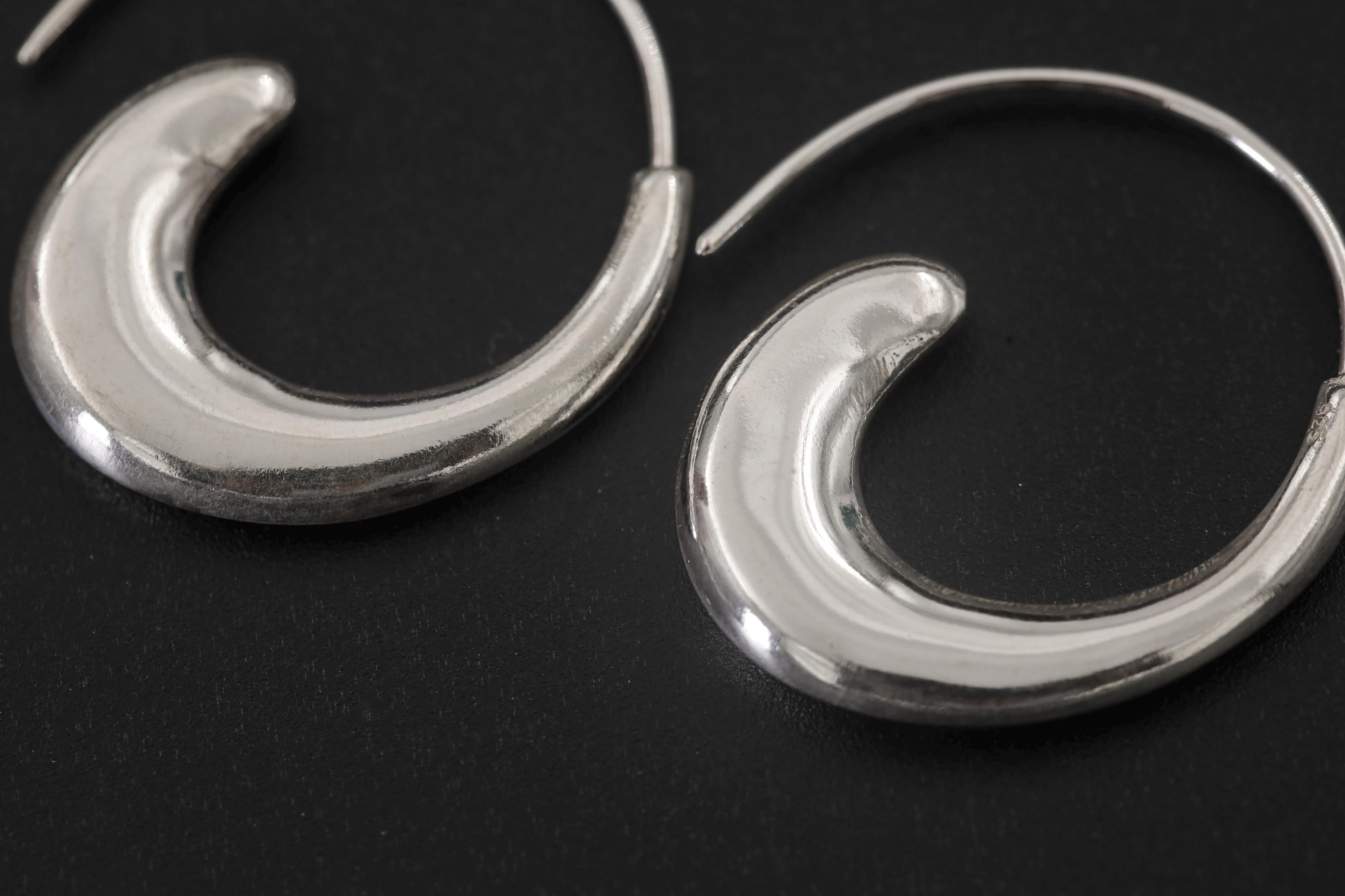 Close view of polished sterling silver wave hoop earrings showing smooth reflective crescent curves.