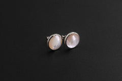 Round Mother of Pearl stud earrings displayed on black background with polished silver settings.