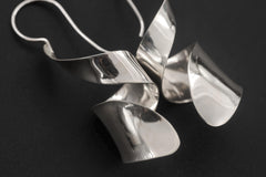 Close view of sterling silver curl earrings showing folded reflective sheet silver form.