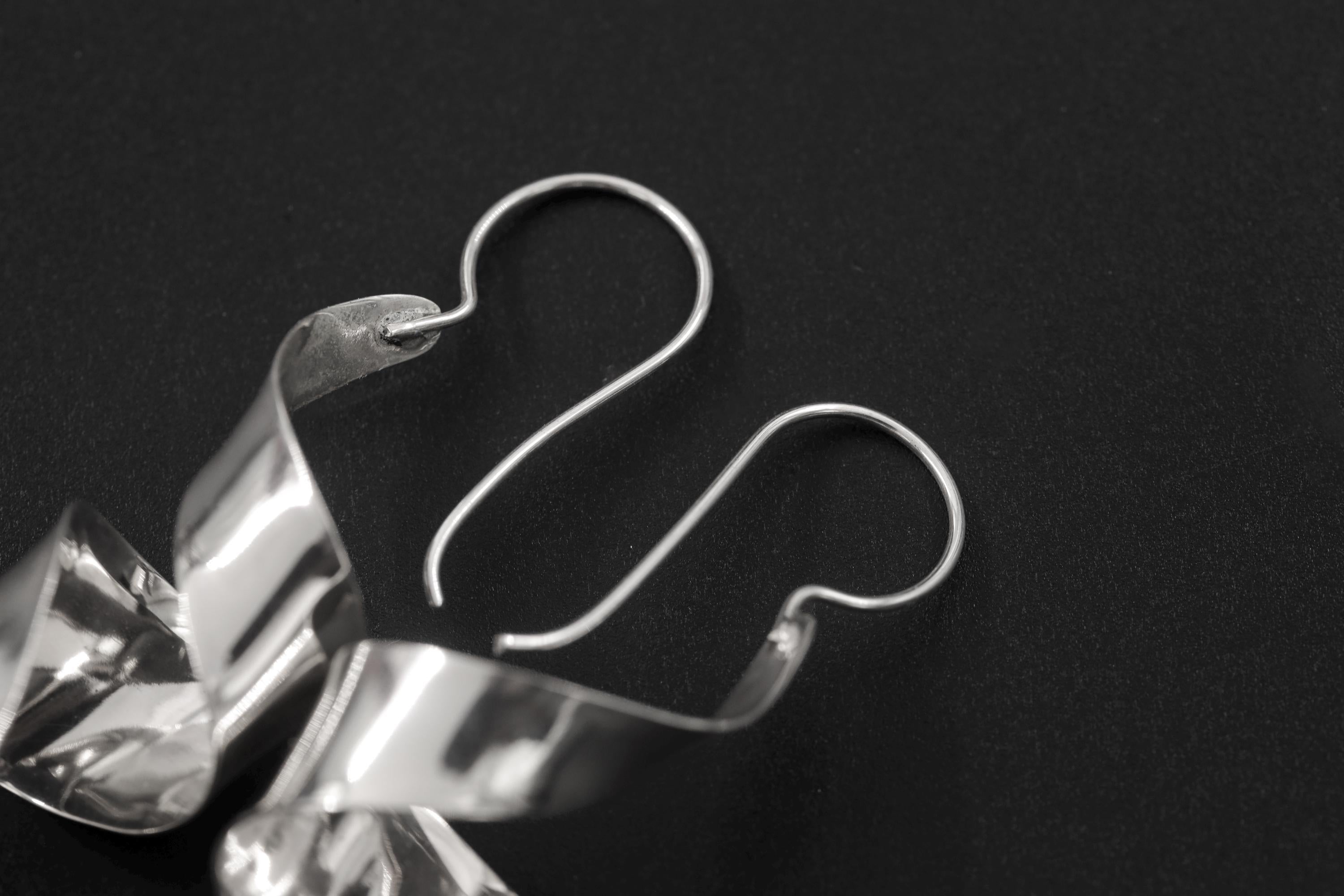 Silver curl earrings displayed on dark background with fish hook ear wires and sculptural movement.