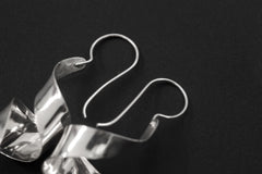Silver curl earrings displayed on dark background with fish hook ear wires and sculptural movement.