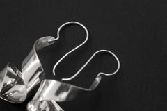 Silver curl earrings displayed on dark background with fish hook ear wires and sculptural movement.