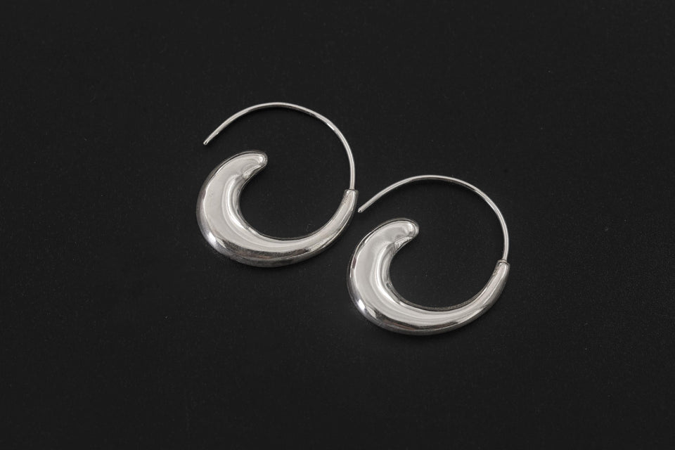 Lunar Tide Wave Earrings displayed on dark background with sculptural crescent silver form.