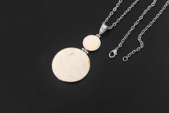 Mother of Pearl pendant displayed on dark background with two circular shell discs and silver chain.