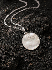 Mother of Pearl disc pendant displayed on dark textured surface with sterling silver chain.