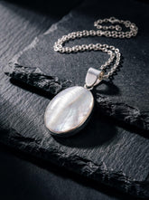 Mother of Pearl oval pendant shown on dark slate with sterling silver chain and soft nacre glow.