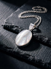 Mother of Pearl oval pendant shown on dark slate with sterling silver chain and soft nacre glow.