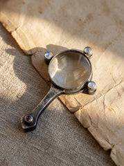Moonstone magnifying glass pendant shown on fabric with blue flash stones and oxidized sterling silver frame.