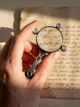 Moonstone magnifier pendant shown held over handwritten paper as a functional oxidized sterling silver lens talisman.