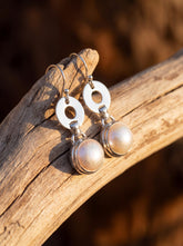 Pearl drop earrings displayed on wood with polished sterling silver circle links and fish hook ear wires.