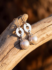 Pearl drop earrings displayed on wood with polished sterling silver circle links and fish hook ear wires.