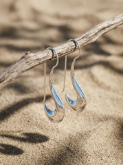 Lunar Crescent Silver Drop Earrings displayed on sand with polished sterling silver moon-shaped drops.