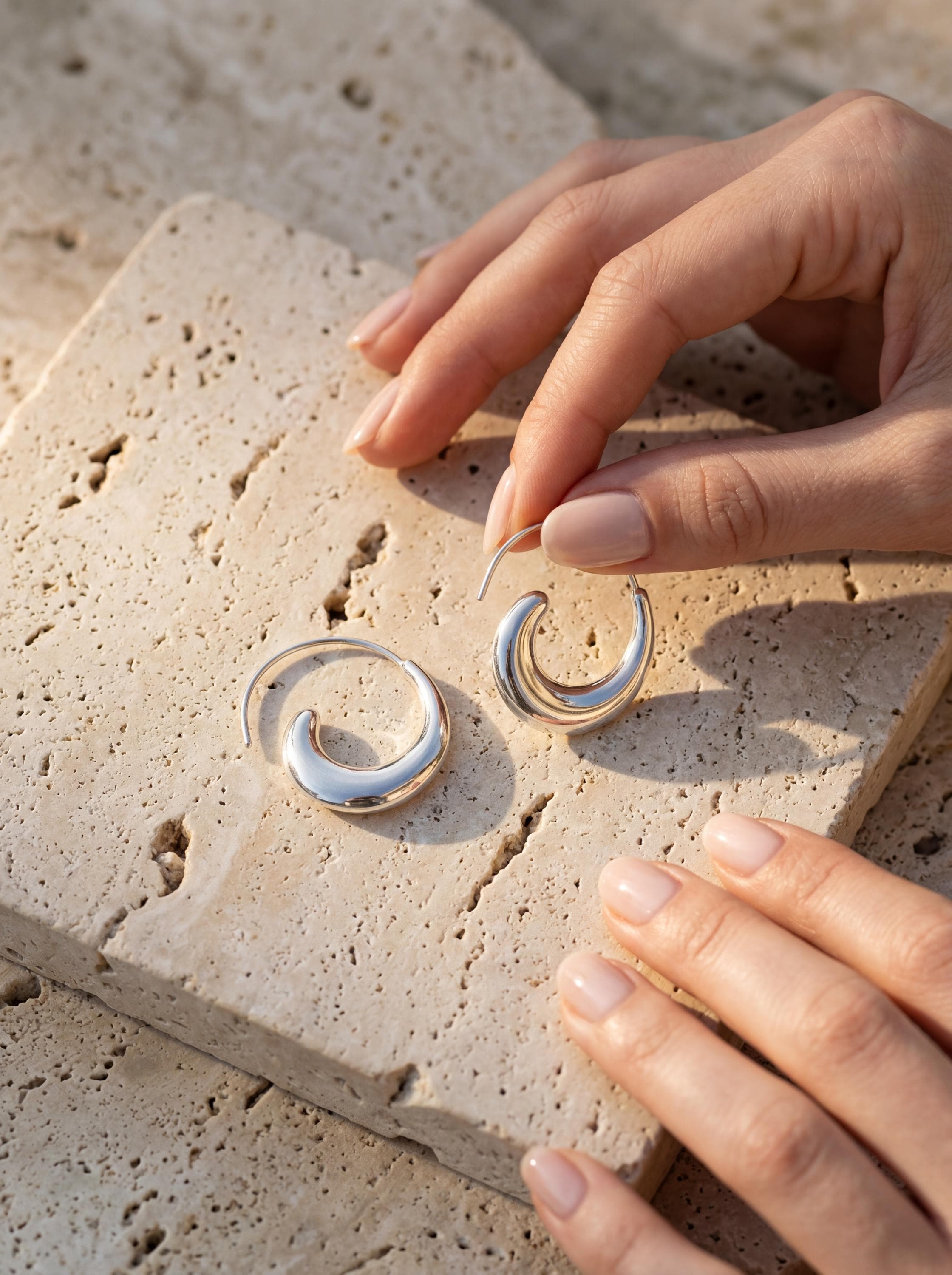 Lunar Tide Wave Earrings displayed on stone with polished sterling silver crescent hoop shape.