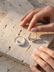 Lunar Tide Wave Earrings displayed on stone with polished sterling silver crescent hoop shape.