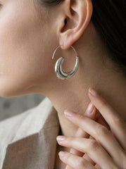 Sterling silver crescent wave earrings shown worn on model as minimalist polished hoops.