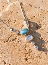 Ocean’s Whisper Radiance necklace shown on sand, with Larimar, Blue Moonstone, Clear Quartz, and sterling silver box chain.