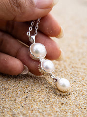 Triple Pearl pendant shown in hand on sand with polished sterling silver and soft nacre lustre.