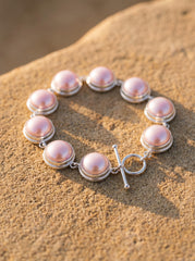 Pink Mabe Pearl sterling silver bracelet displayed on sand with soft blush Pearl glow.