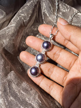 Black Pearl triple drop pendant shown in hand with polished sterling silver settings and dark iridescent pearls.