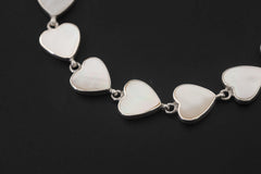 Close view of Mother of Pearl heart bracelet showing white shell cabochons in polished silver bezels.