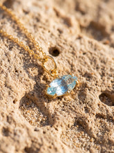 Blue Topaz eye pendant displayed on sand with gold-plated sterling silver and pale blue marquise stone.