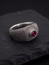 Garnet oxidized sterling silver ring displayed on dark slate with textured signet band and red gemstone.