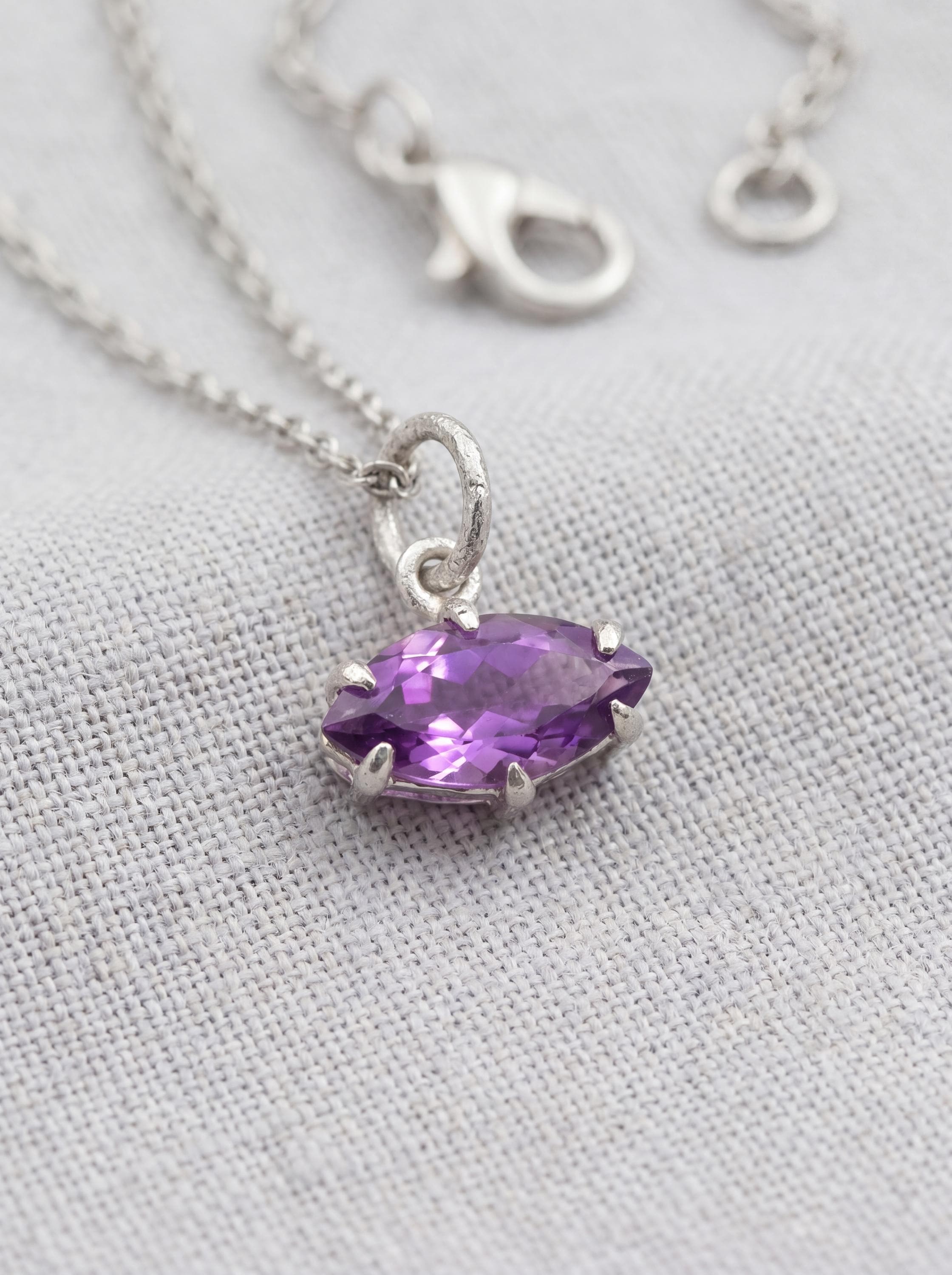 Faceted Amethyst marquise pendant shown on linen with sterling silver claw setting.