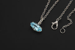 Blue Topaz marquise pendant displayed on sand with sterling silver chain and bright sky-blue stone.