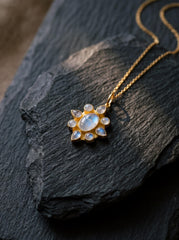 Blue Moonstone flower pendant shown on a dark stone surface, with gold-plated sterling silver and luminous petal-shaped stones.