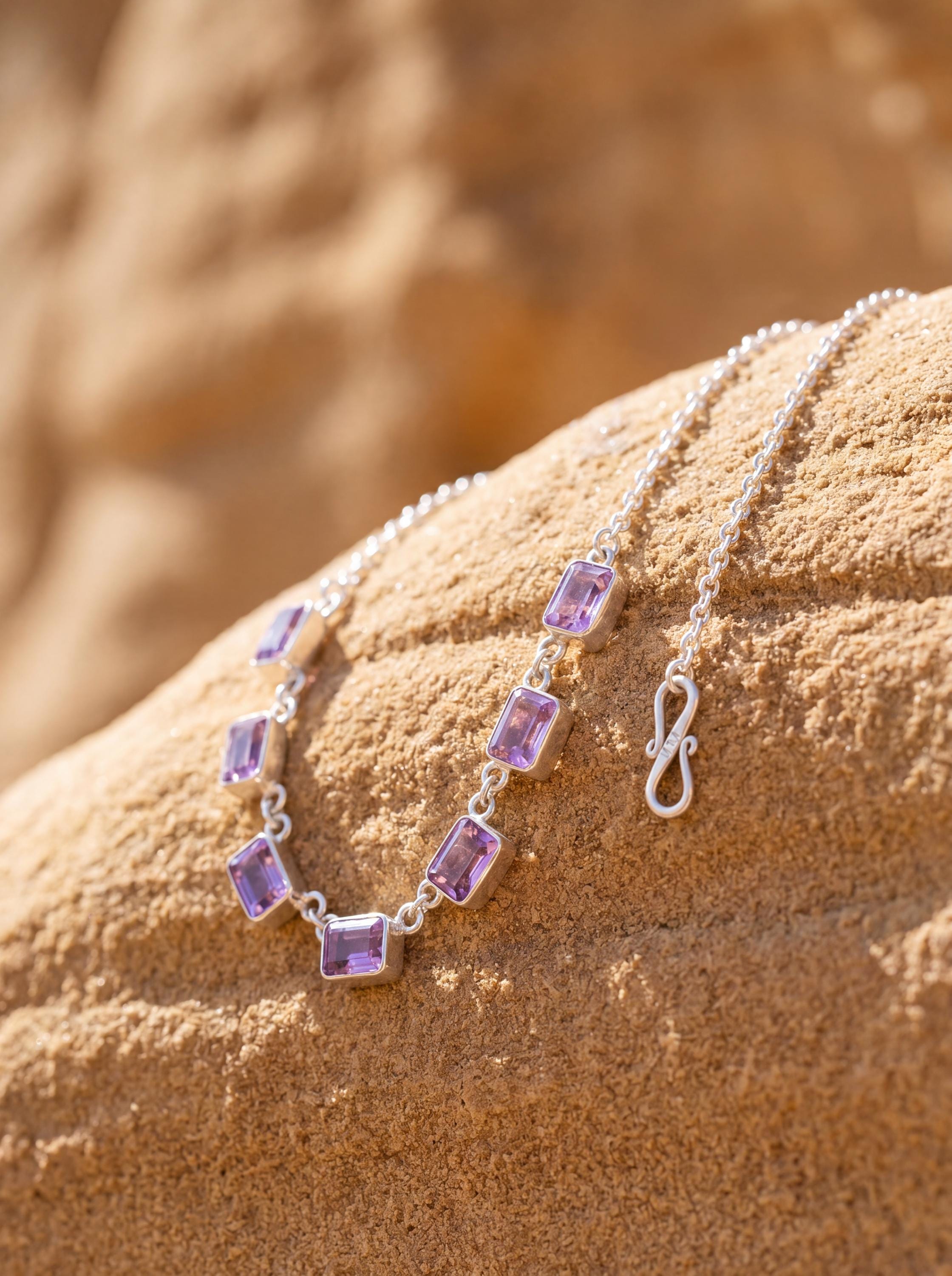 Amethyst sterling silver necklace shown on sand with seven square purple gemstones and fine silver chain.