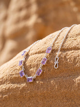 Amethyst sterling silver necklace shown on sand with seven square purple gemstones and fine silver chain.