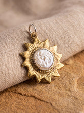 Gold-plated brass sun pendant with round Mother of Pearl centre, shown on textured fabric as a celestial lunar talisman.