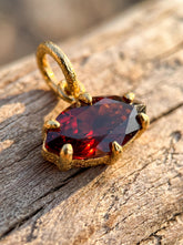 Gold-plated Garnet pendant shown on natural wood with deep red marquise stone and claw setting.