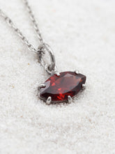 Faceted Garnet marquise pendant shown on light fabric with sterling silver claw setting.