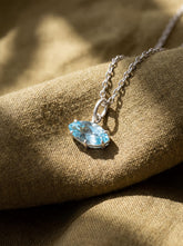 Faceted Blue Topaz marquise pendant shown on linen with sterling silver claw setting.