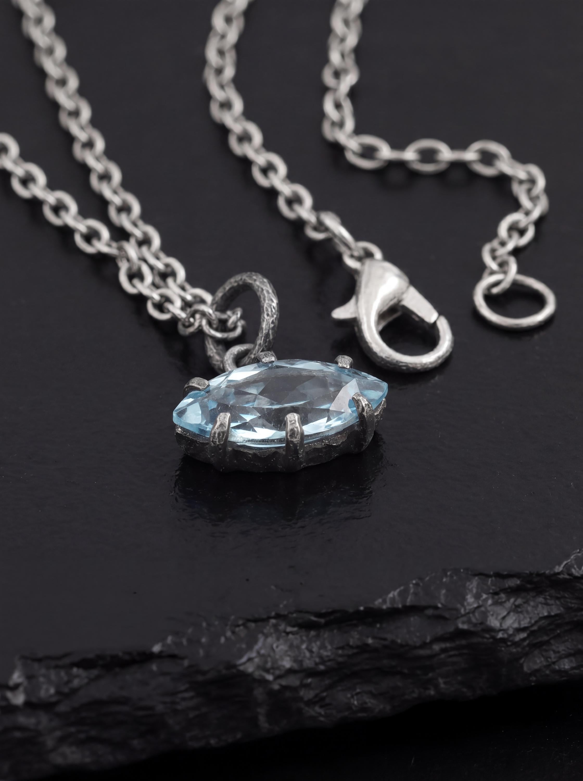Blue Topaz eye pendant displayed on dark slate with oxidized chain and textured silver setting.