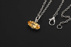 Citrine marquise pendant displayed on sandstone with chain and warm golden light.