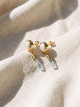 South Sea Pearl and raw Aquamarine gold-plated sterling silver stud drop earrings shown on soft fabric.