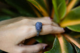 Handmade 925 sterling silver raw Tanzanite ring shown worn on the hand, with blue-violet stone and fine silver band.