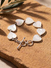Mother of Pearl heart bracelet shown on warm textured surface with polished sterling silver toggle clasp.