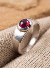 Garnet cabochon sterling silver ring displayed on linen with polished band and deep red stone.