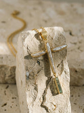 Baroque Pearl Aquamarine cross pendant in 18k gold-plated sterling silver shown on Quartz, with raw Pearl texture and blue-green dangle.
