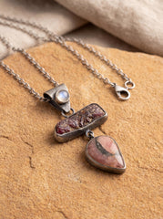 Multi-stone pendant displayed on sand with Moonstone, Raw Ruby, Rhodochrosite, and oxidized silver chain.