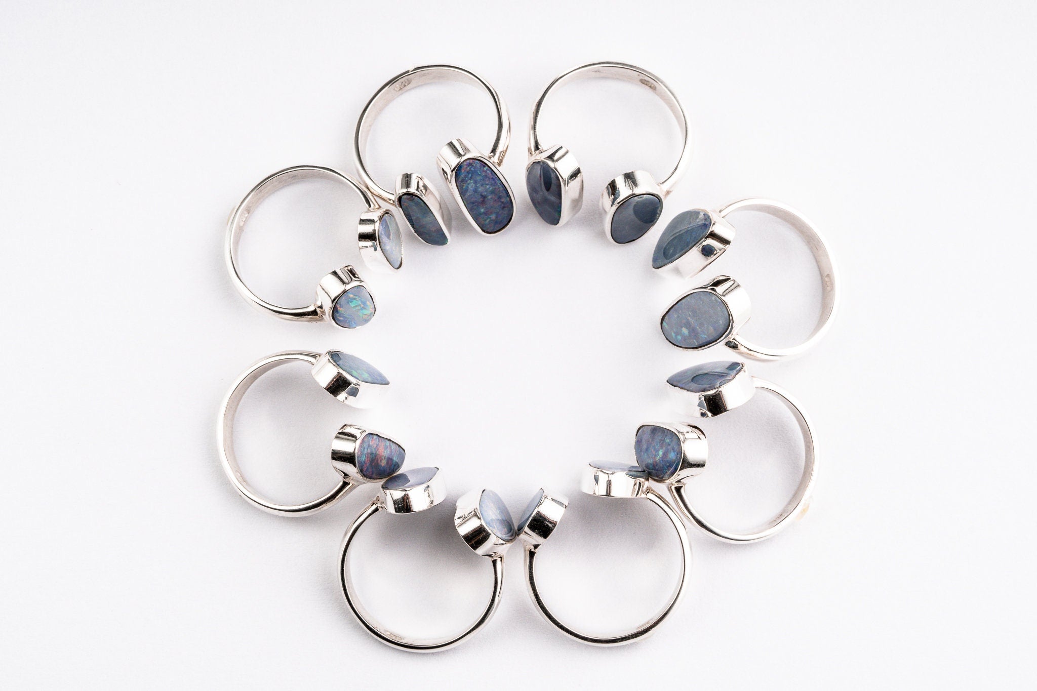Australian Opal Doublet Adjustable Rings shown arranged in a circle with sterling silver open bands and luminous stones.