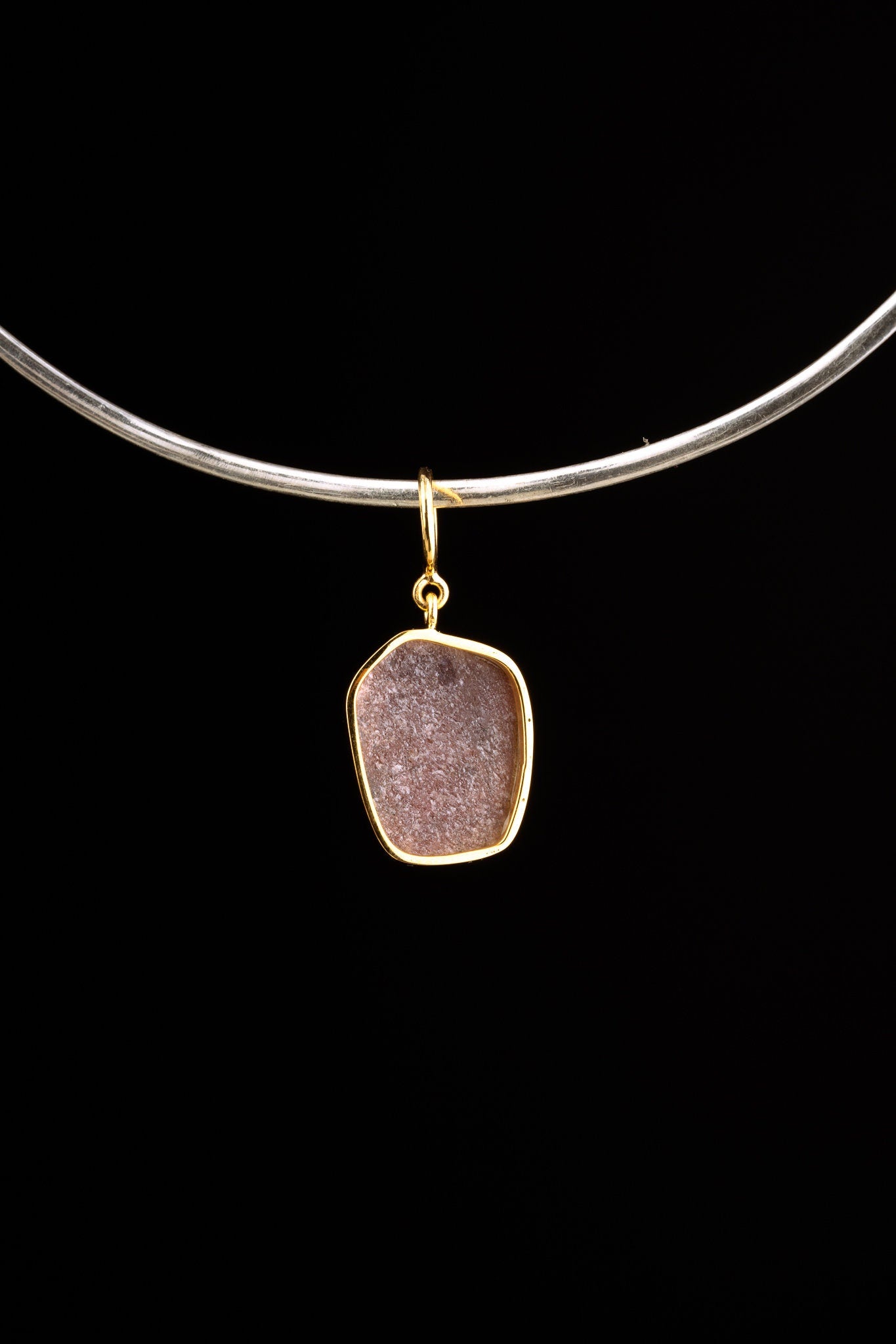 Compact raw Ruby pendant shown worn on a black cord, with warm gold-plated setting and natural mineral inclusions.