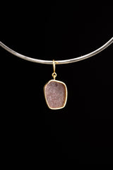 Compact raw Ruby pendant shown worn on a black cord, with warm gold-plated setting and natural mineral inclusions.