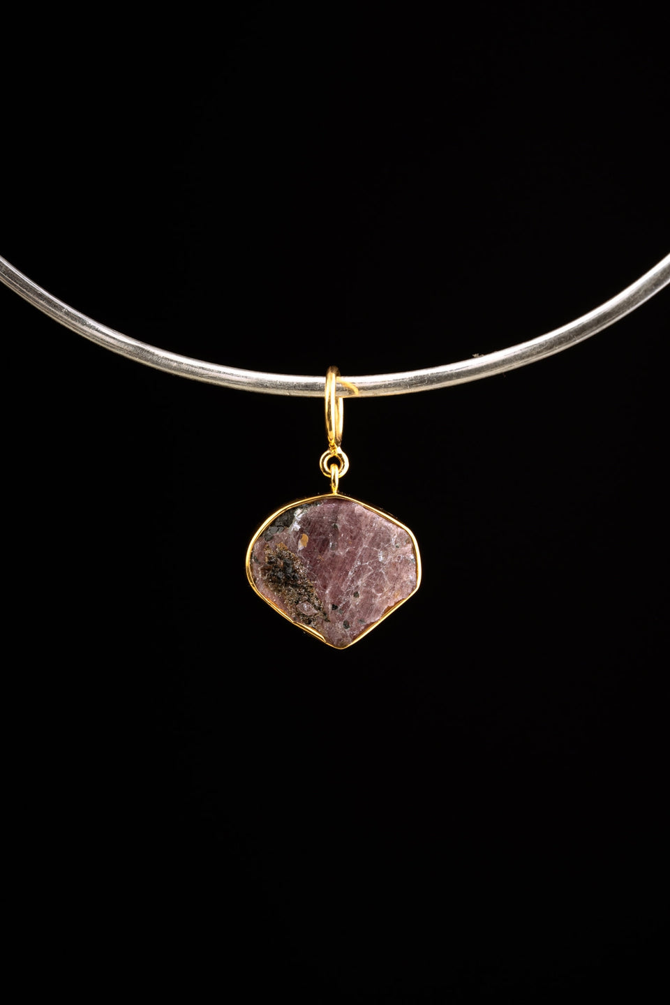 Raw Ruby pendant shown on a black cord, with warm gold-plated silver setting, wide bail, and earthy red mineral texture.