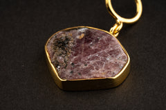 Compact raw Ruby pendant shown worn on a black cord, with 16k gold-plated setting and natural mineral inclusions.