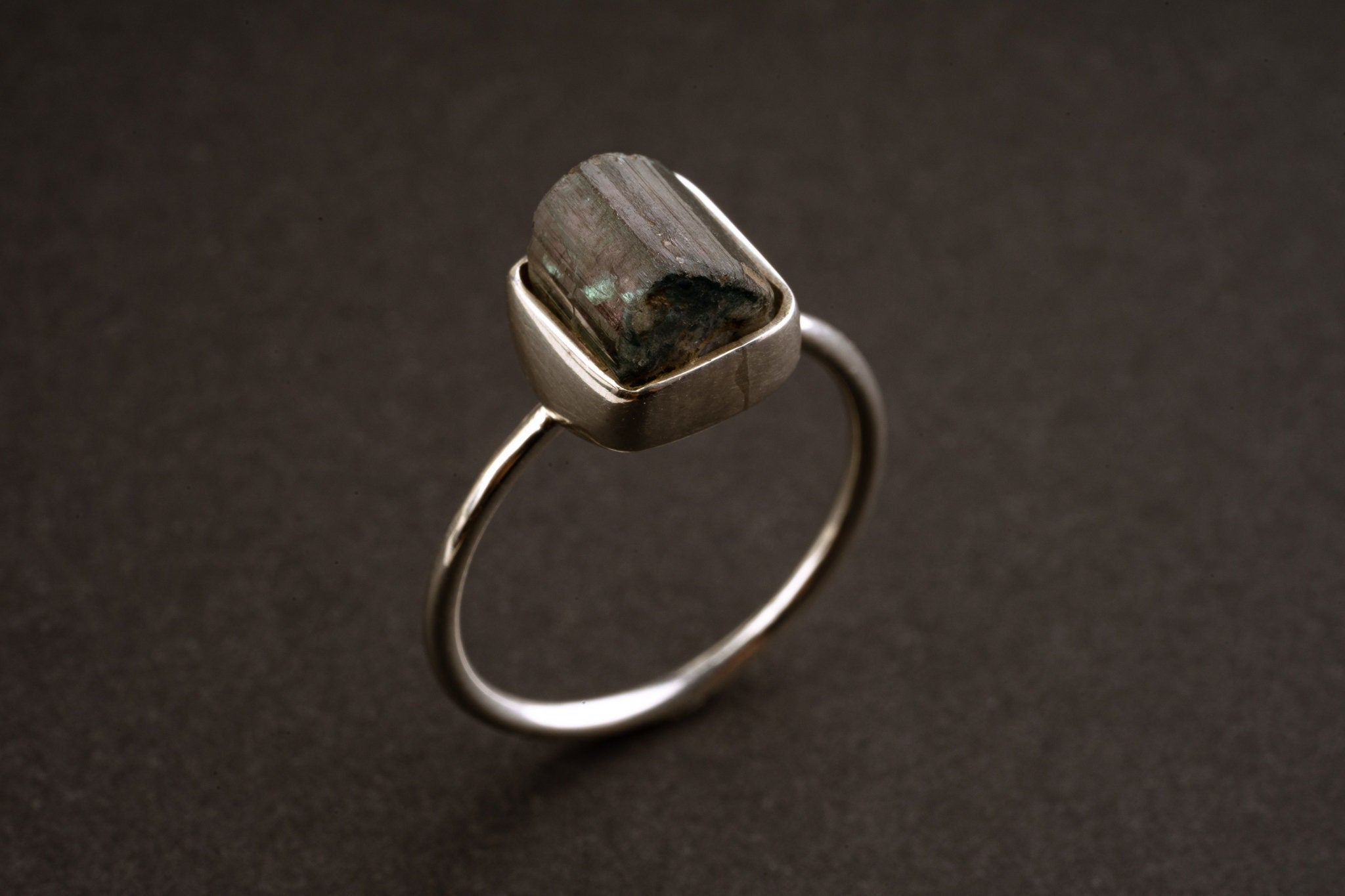 Watermelon Tourmaline sterling silver stack ring shown on a dark background, with rough crystal and fine silver band.